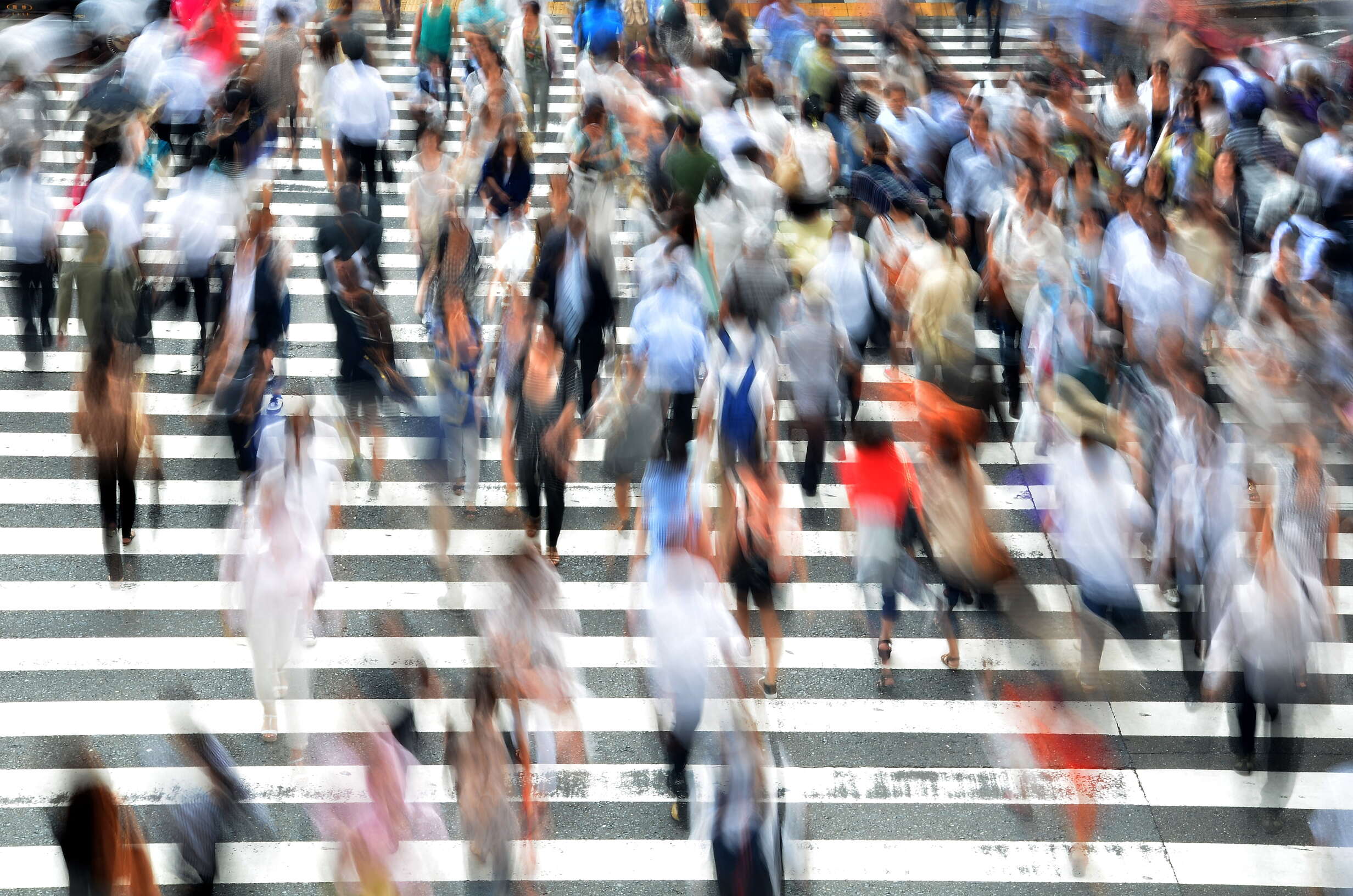 A crowd of people, blurred by a long exposure, move through a busy crosswalk