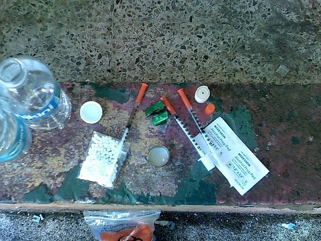 2. Syringe, cooker, and water on top of an improvised table at a shooting gallery