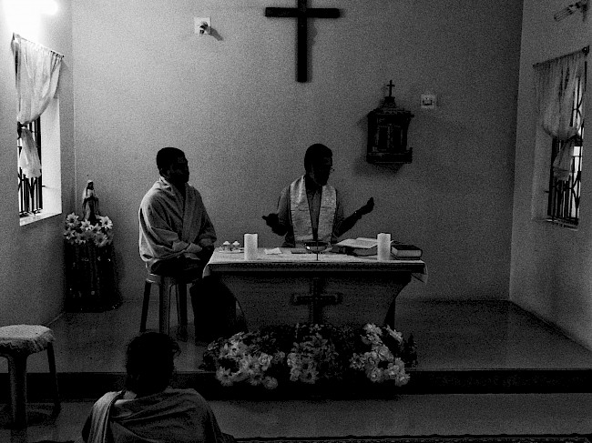 Figure 3. The morning prayer session (at 05:00 every day) is held in a separate building where the Fathers have their lunch. In this image, Father Judy and Father Jose read the sermon, while a Sister sits and listens in the foreground.