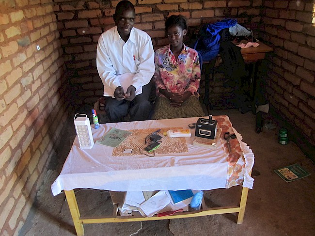 Photograph 9: Tailor (35) with his wife, surrounded by their possessions at their workshop